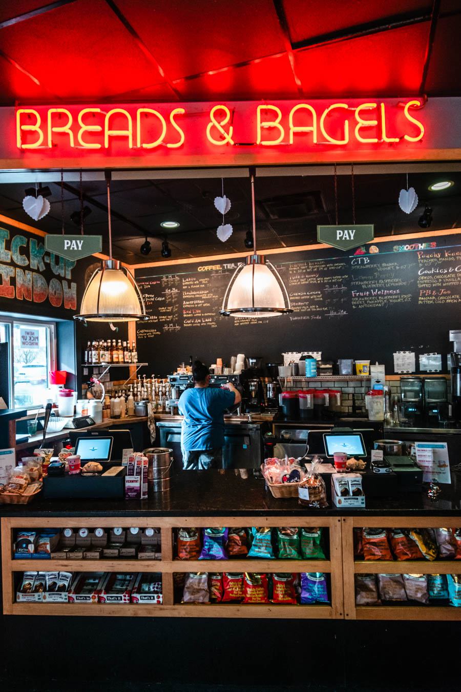 Image of a café with a neon sign reading "Breads & Bagels" – A cozy café with a chalkboard menu and a barista preparing coffee, illuminated by warm lighting, perfect for a winter morning in the Finger Lakes.