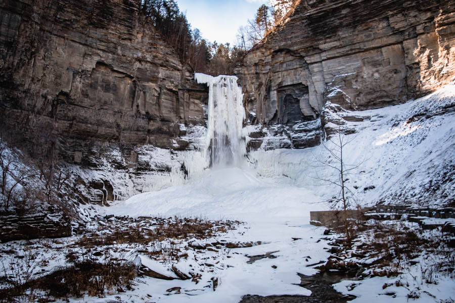 Image of a towering frozen waterfall with a snowy landscape – The iconic Taughannock Falls partially frozen in winter, surrounded by dramatic rock cliffs and a snow-covered gorge.