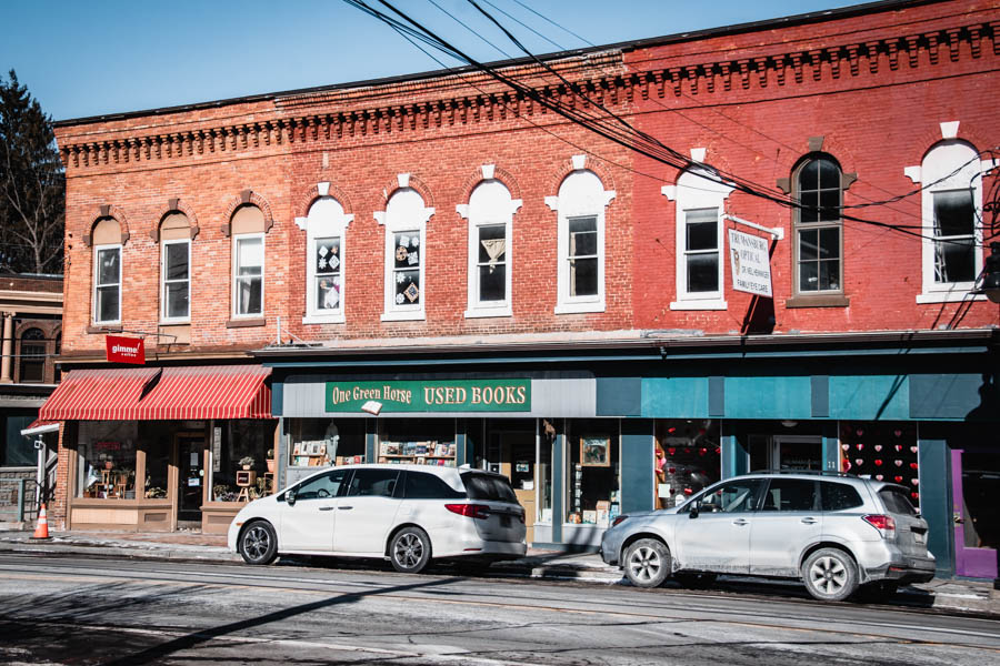 Image of a red brick building with shops, including a used bookstore and a café – A charming historic brick building with local businesses, including "One Green Horse Used Books" and "Gimme! Coffee," on a winter day in the Finger Lakes.