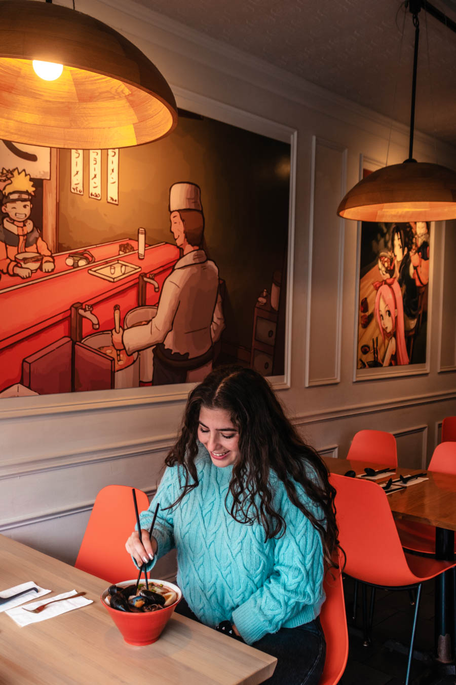 Traveler enjoying a bowl of ramen in a colorful anime-themed restaurant, savoring a warm meal on a winter day.