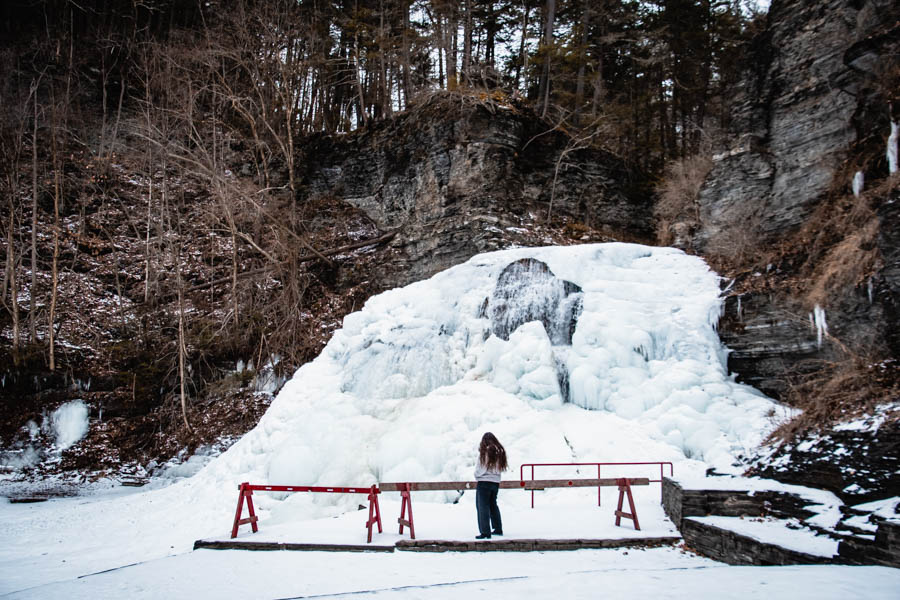 Taking in the beauty of a frozen waterfall – A woman standing at a red railing, gazing at the layers of ice and snow cascading down a rock face.