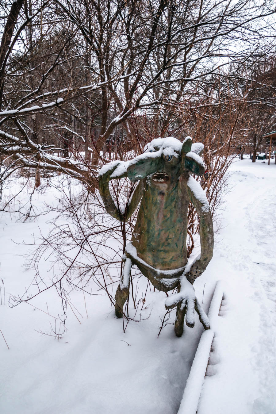 A whimsical sculpture of a snow-covered troll in a wintery wooded park, adding a magical touch to an outdoor adventure.