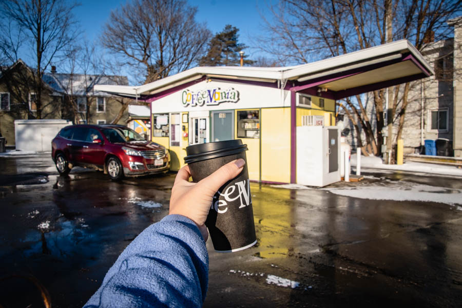 A hand holding a takeaway coffee cup from Coffee Mania, a popular local drive-thru coffee stop in the Finger Lakes.