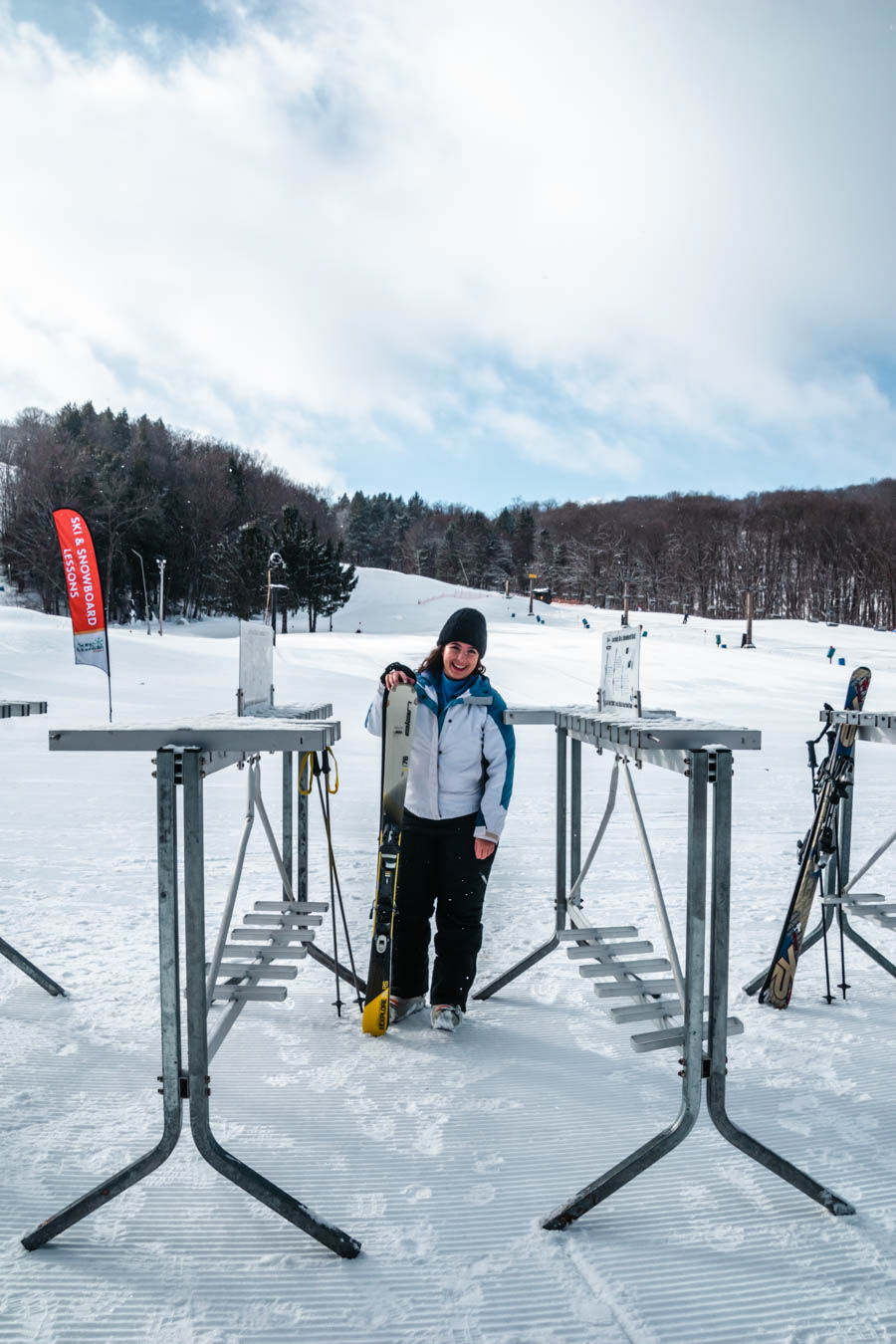 A woman in a ski jacket and hat standing at a ski rack, ready for a fun day on the slopes in the Finger Lakes at Song Mountain Resort