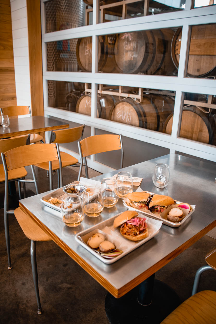 Image of a table with sandwiches, cider glasses, and small plates at South Hill Cider – A delicious spread of artisanal sandwiches, wine, and small bites at a Finger Lakes cidery, set against a backdrop of stacked barrels.