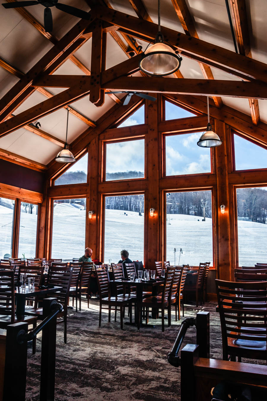 Inside a Cozy Ski Lodge with Mountain Views – A rustic dining area inside a ski lodge, featuring wooden beams, large windows, and breathtaking snowy mountain views.