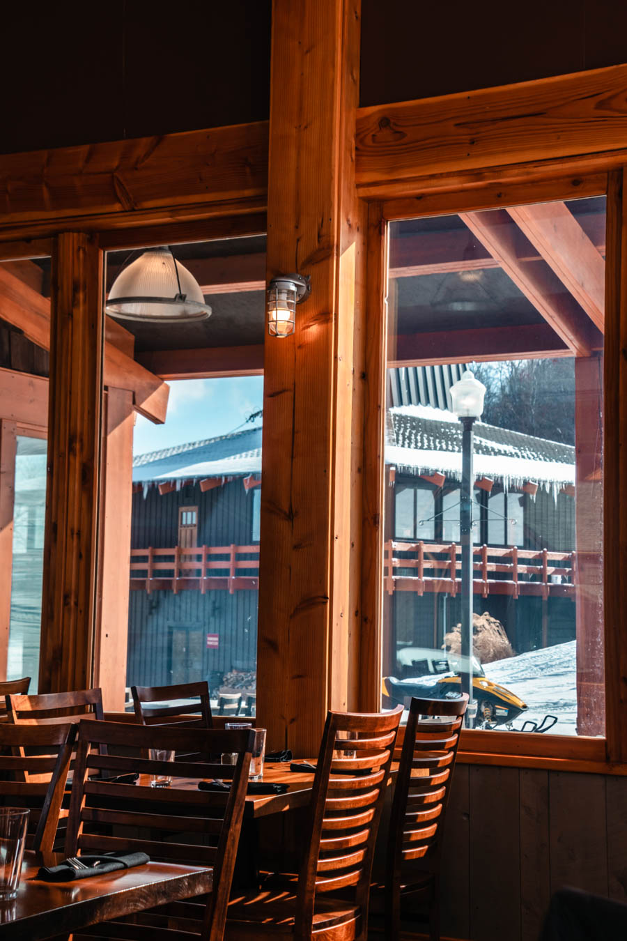 Inside a Cozy Ski Lodge with Mountain Views – A rustic dining area inside a ski lodge, featuring wooden beams, large windows, and breathtaking snowy a building views.