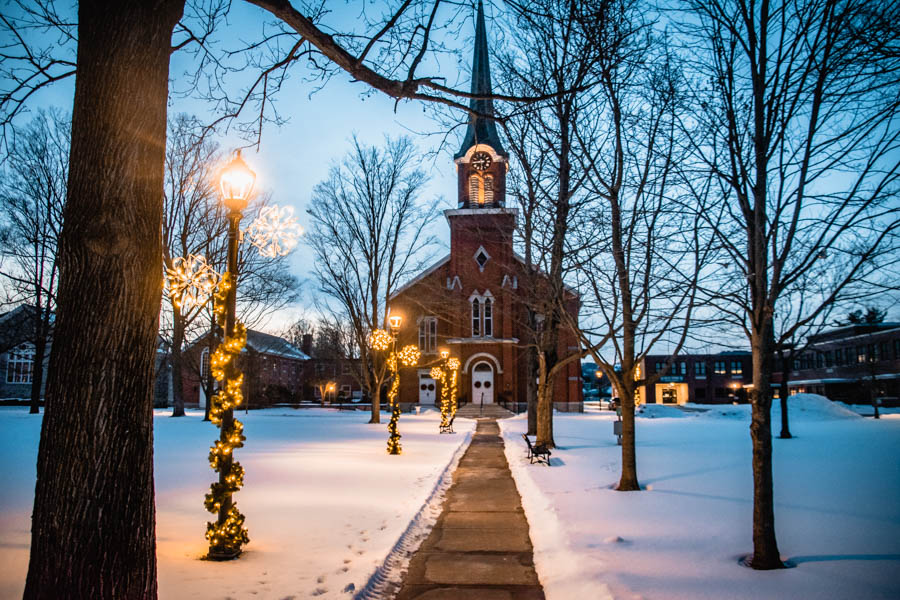 Fairy-Tale Winter Church at Dusk – A charming red-brick church with twinkling lights, surrounded by snow and trees, creating a magical winter scene.