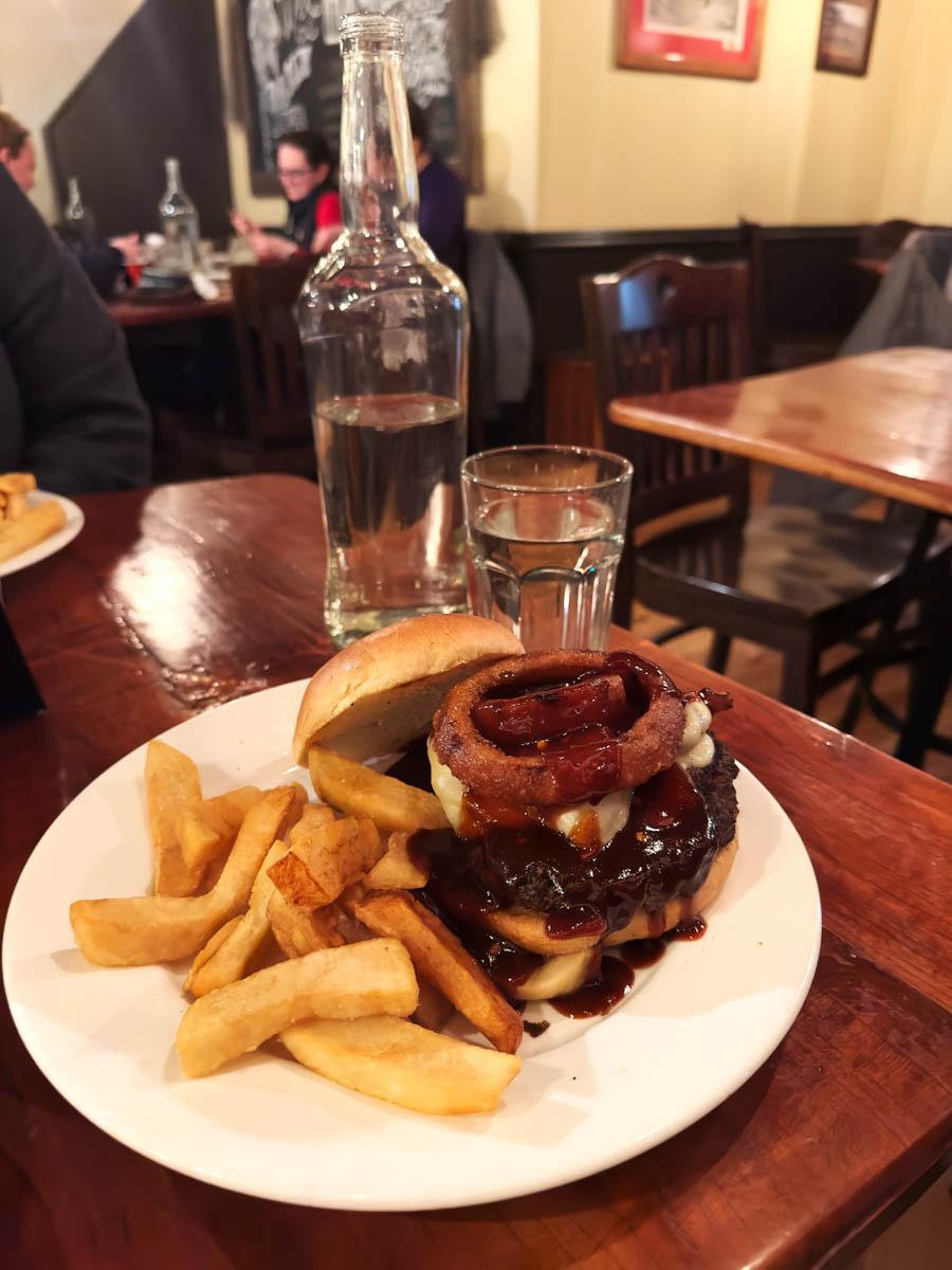 BBQ bacon burger with thick-cut fries – A hearty meal featuring a juicy BBQ bacon burger topped with onion rings, served with golden fries.