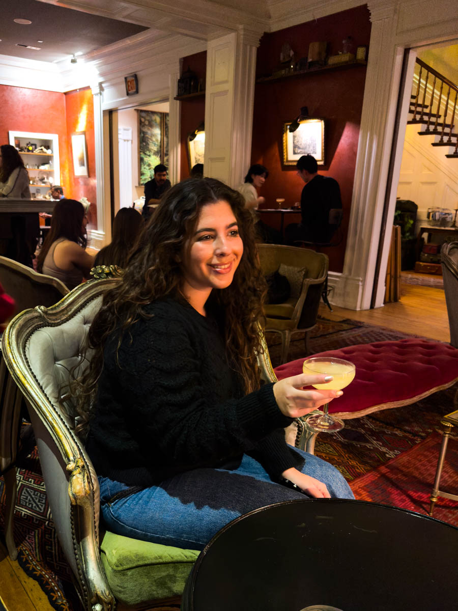 Enjoying cocktails at Bar Argos – A woman with long curly hair smiles as she holds a cocktail in the stylish and warmly lit Bar Argos.